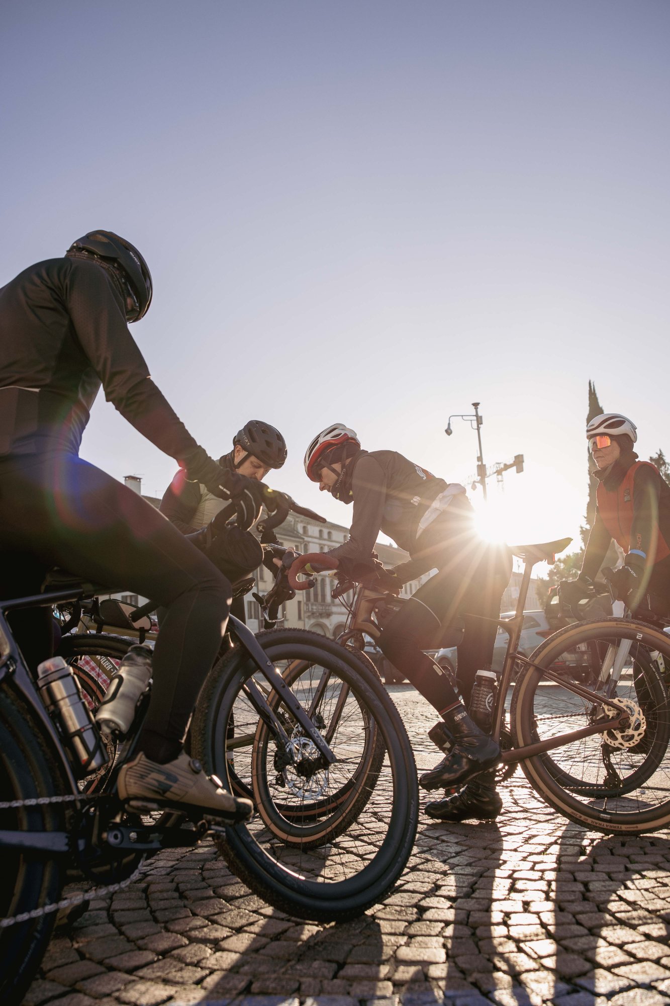 Ciclisti gravel alla partenza dell'evento Adelante Experience nel centro storico veneto con luce dorata del tramonto
